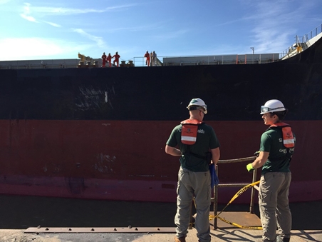 Green vests standing by dock near big ship