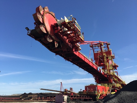 Large red crane hoisting coal from the earth