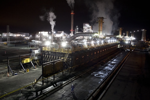Large industrial plant at night with smoke billowing out of the chimneys