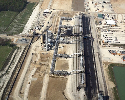 Large industrial plant with smokestacks emitting steam, surrounded by machinery and pipeline